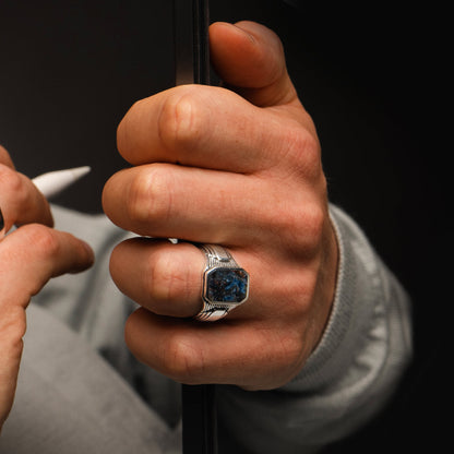 A man is holding white pen and a book while wearing Bariq sterling silver mens signet ring by NineTwoFive.